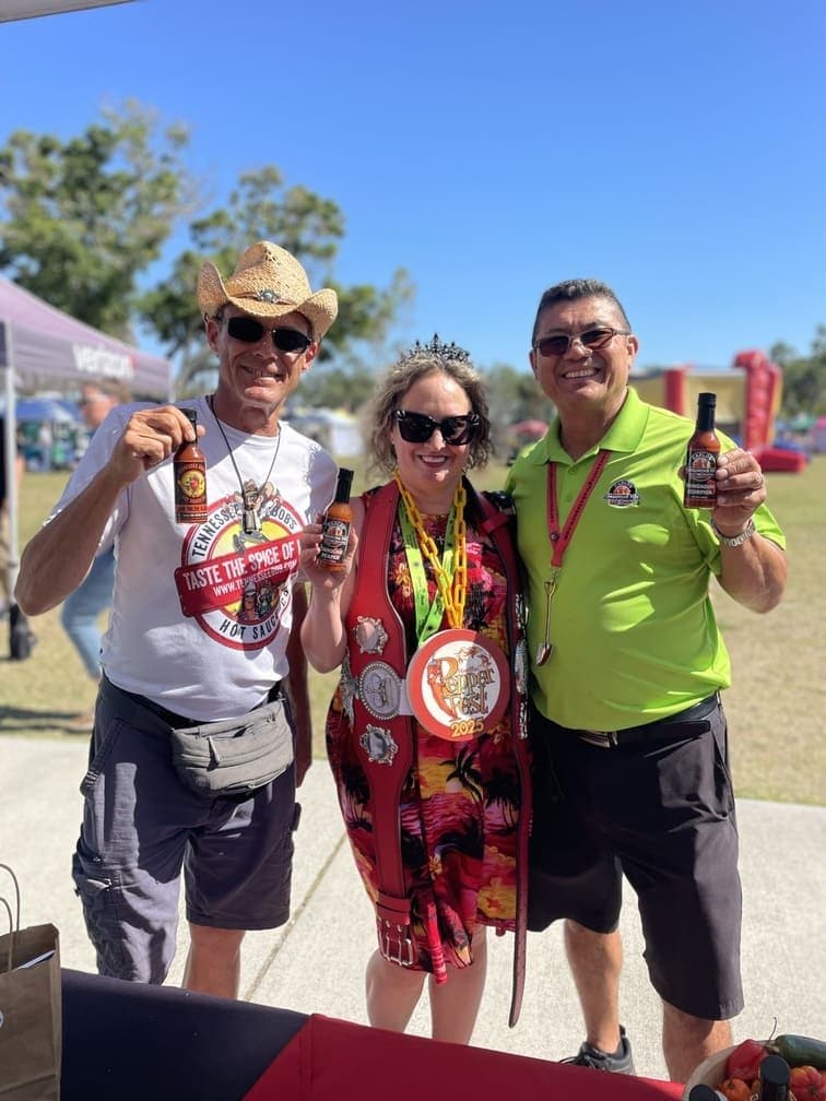 Three people posing with hot sauce bottles at Pepper Fest 2025; Carlos, in the green Tennessee Bob's polo shirt, stands on the right.