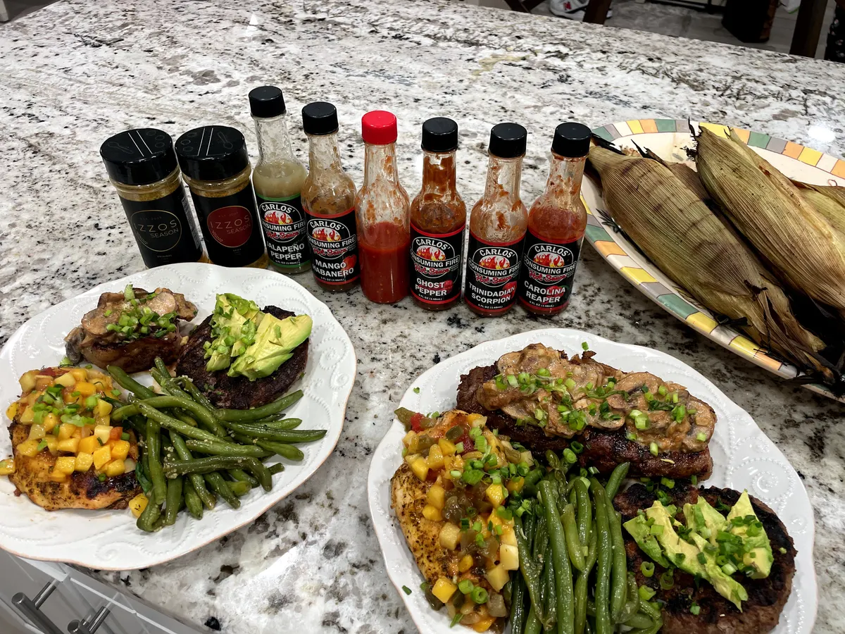 Grilled dinner plates and charred corn with the Ghost Pepper Hot Sauce bottle in the five-sauce lineup